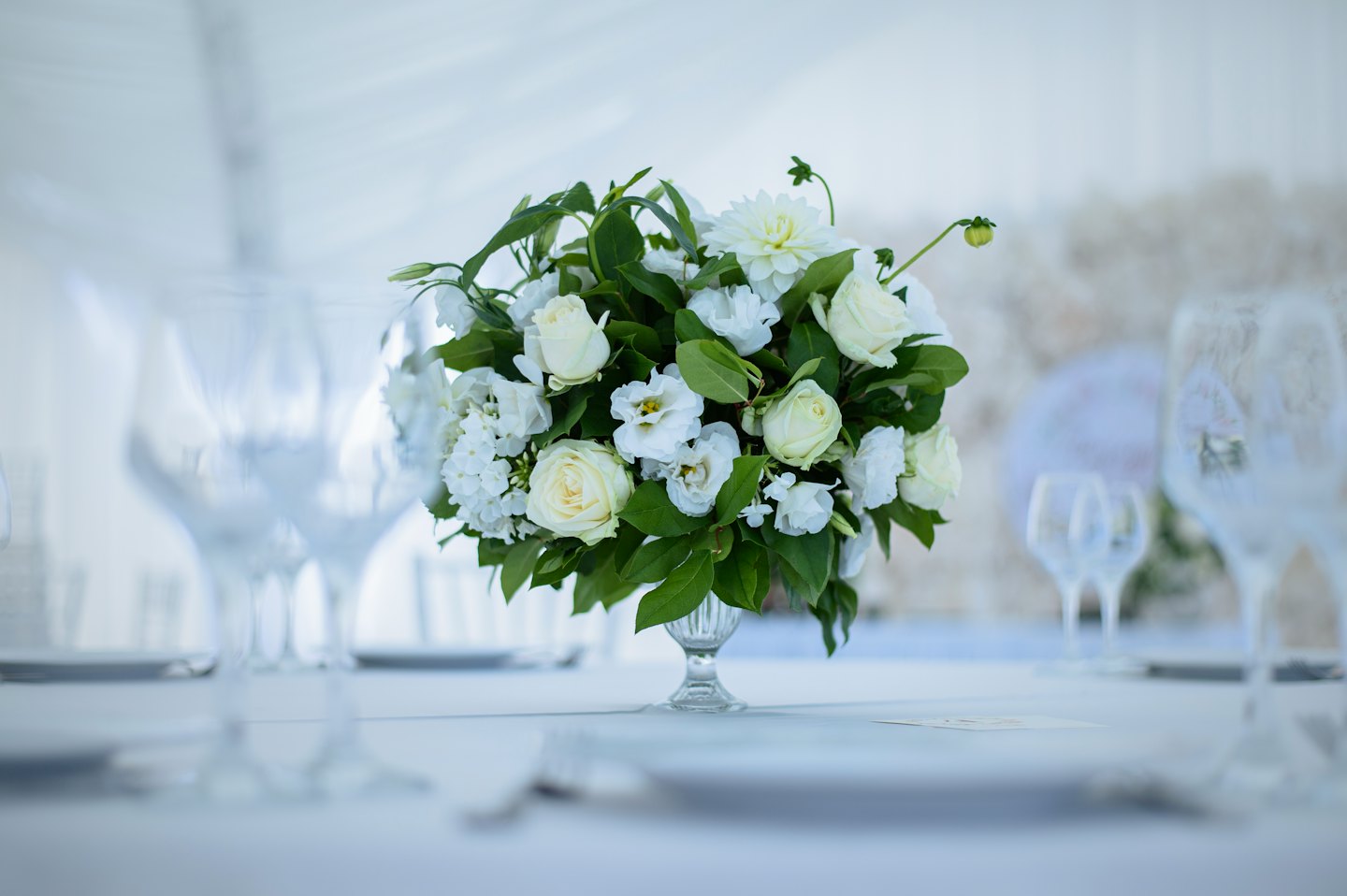 Elegant white floral centerpiece with roses and dahlias on a table.
