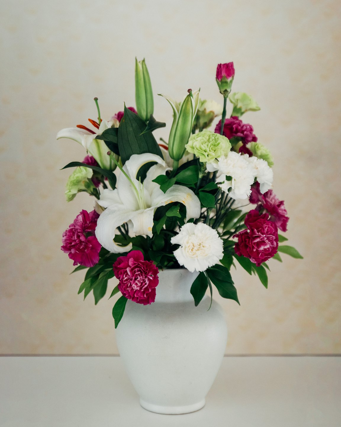 White lilies and carnations in a white vase.