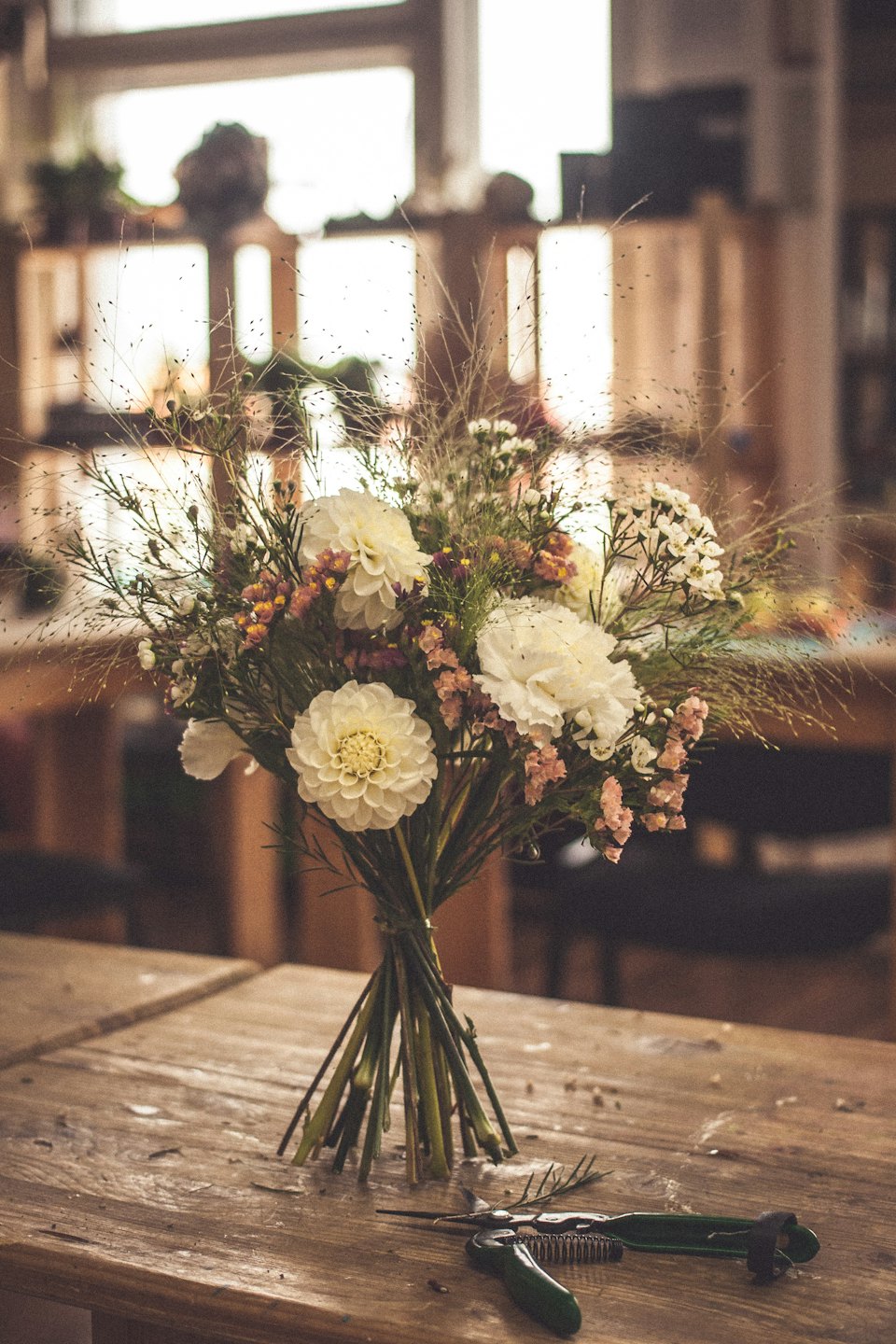 White dahlias and floral tools on a rustic wooden table.