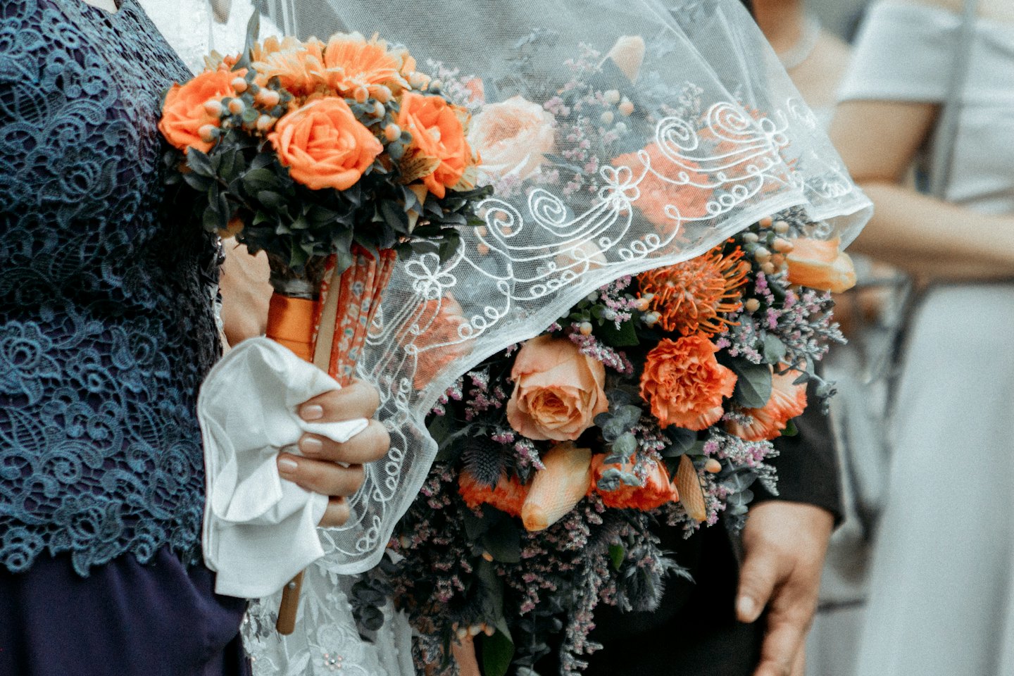 A hand holds a colorful floral bouquet draped in lace.