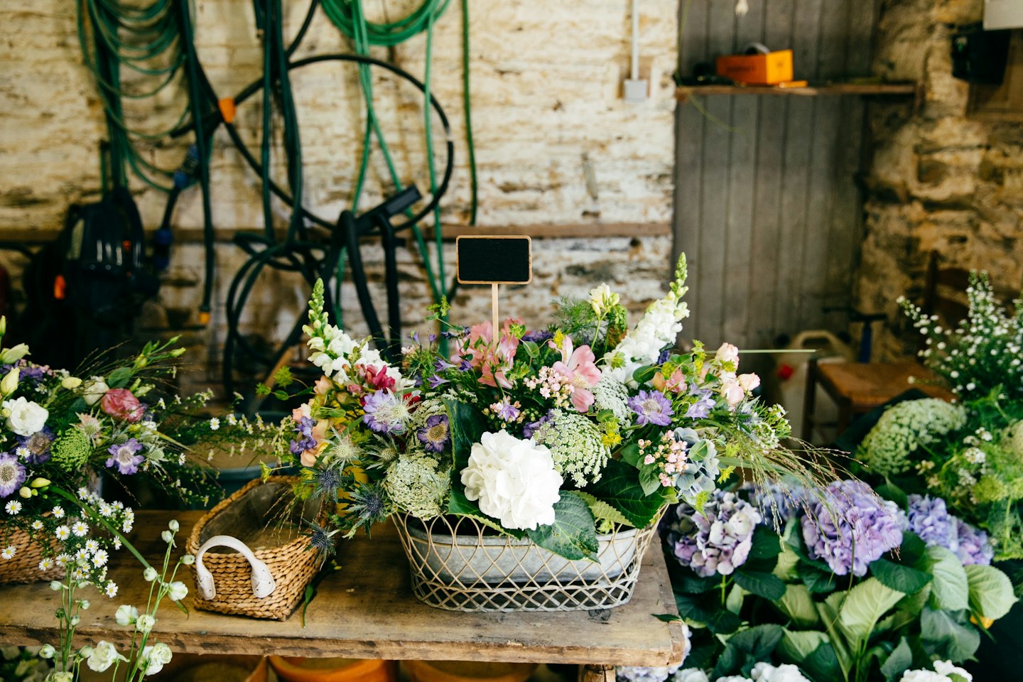 Mixed floral arrangements on a rustic wooden table with a blackboard sign.